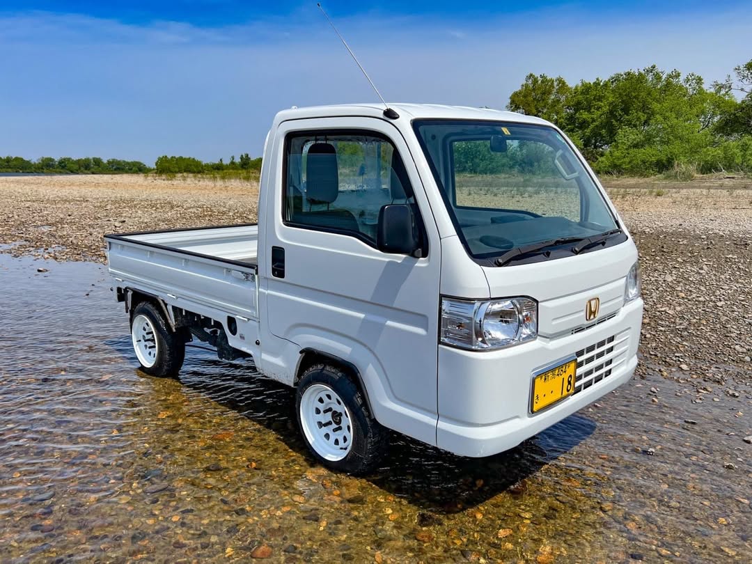 White Honda Acty HA8, HA9 (2009-2022) kei truck with white wheels parked on a rocky riverbed, showcasing its off-road capability and compact utility design.